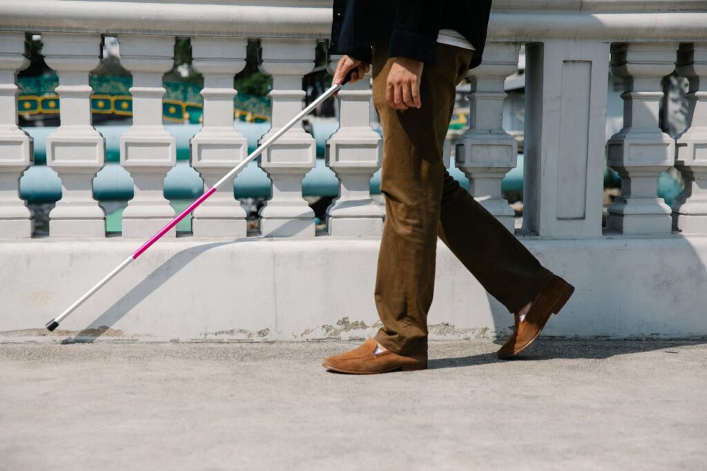 A blind man walking confidently outdoors with a white cane for navigation.
